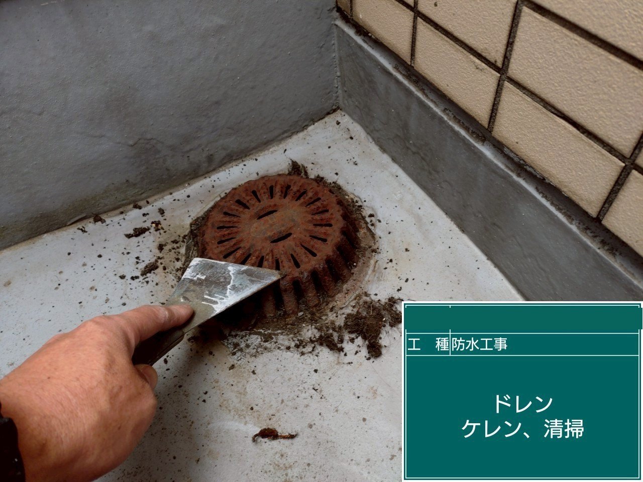 バルコニーの排水口まわりの錆と汚れをへらで削っている様子