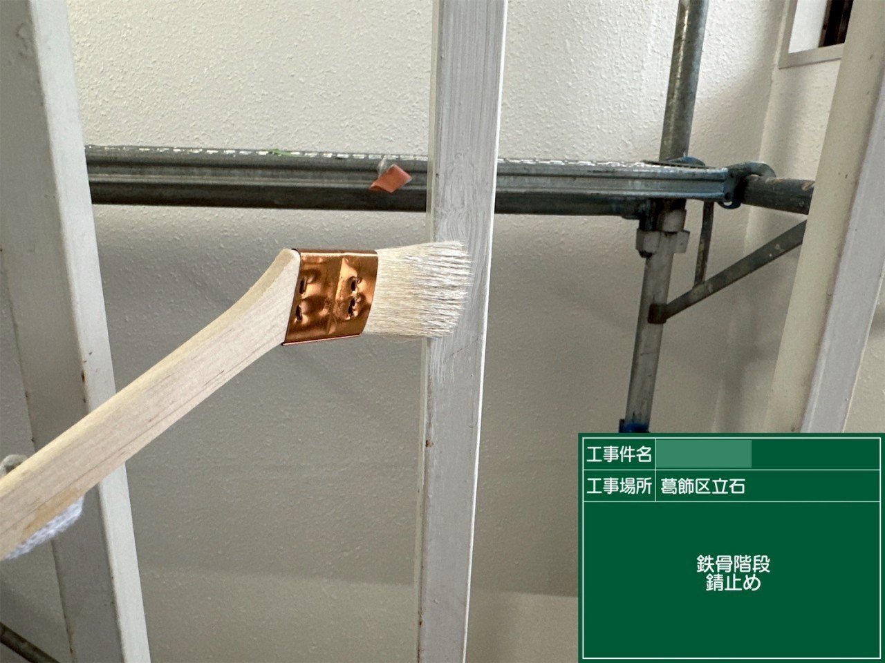 鉄骨階段の部材に錆止めを刷毛で塗っている様子